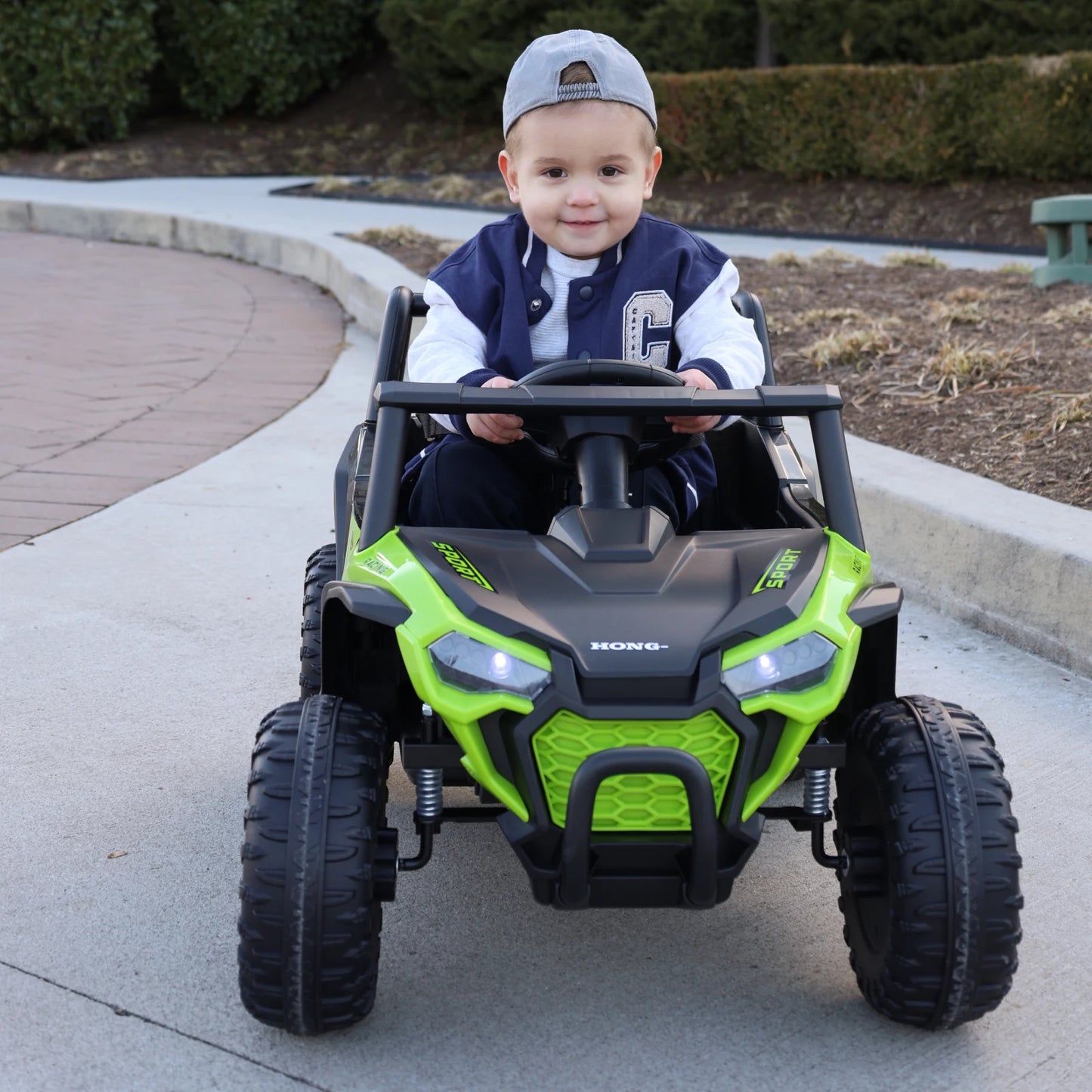 Child driving a green toy off-road vehicle on a sidewalk