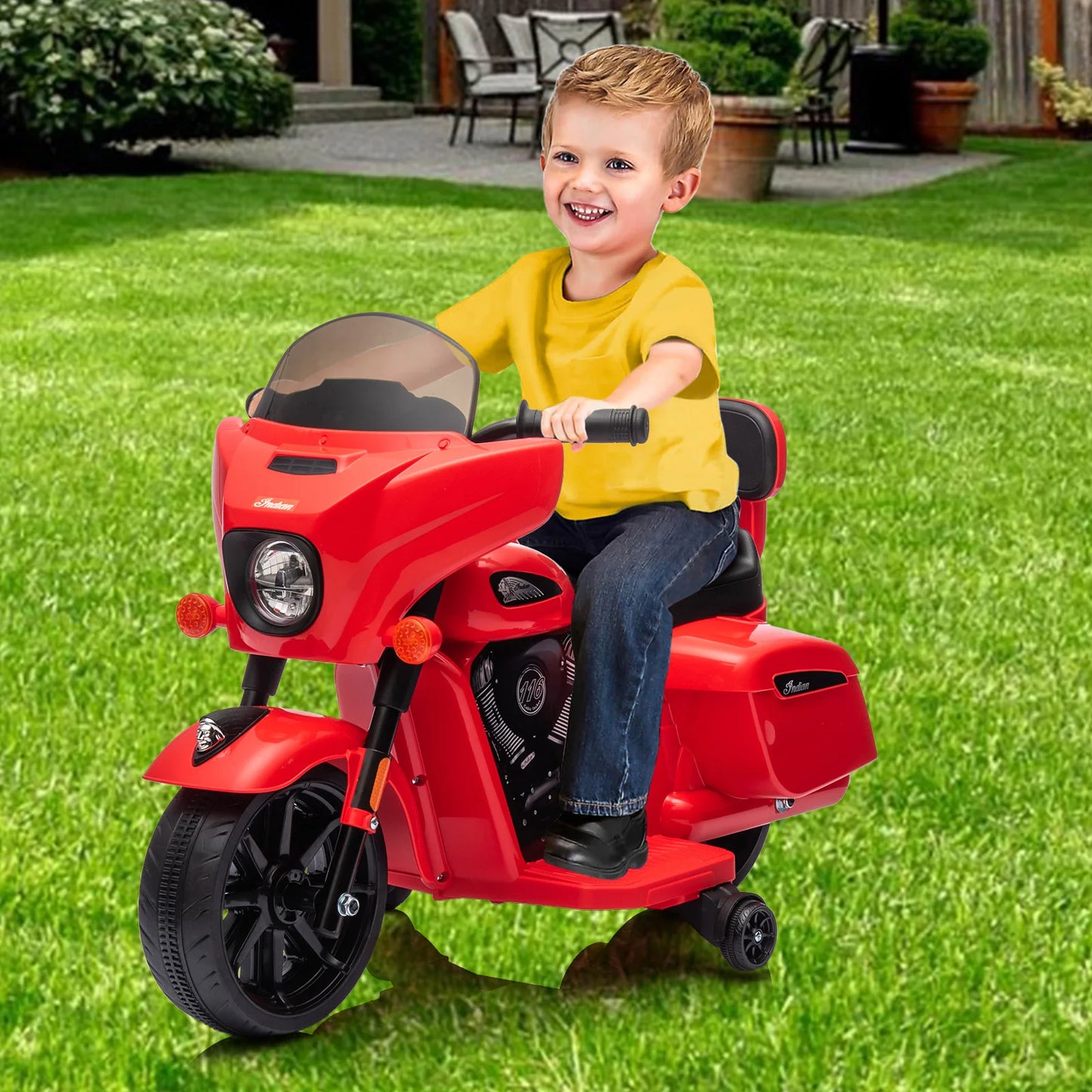 Child sitting on a red toy motorcycle in a grassy outdoor area