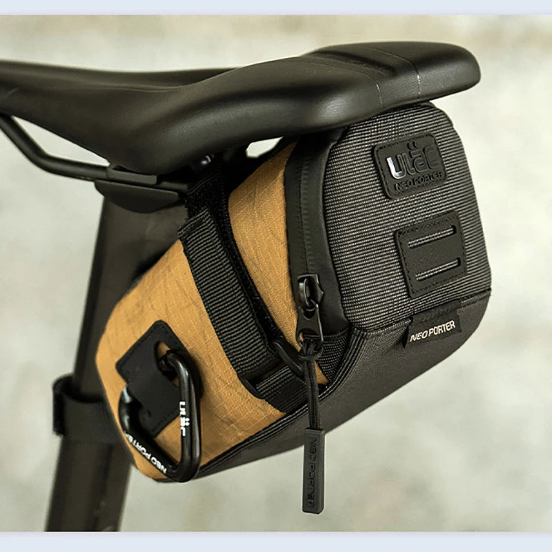 Brown and black saddle bag attached to a bicycle seat with a blurred background